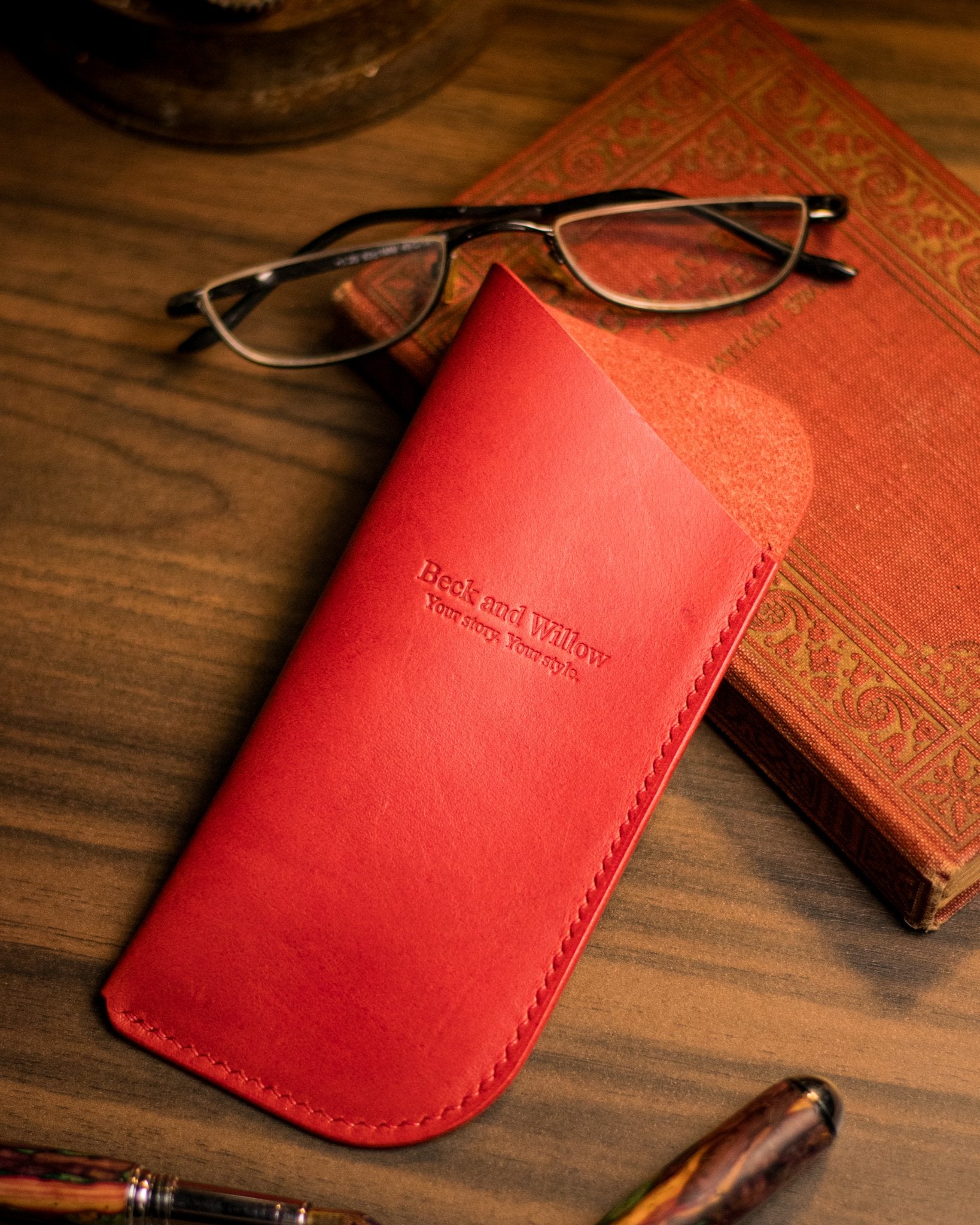 Lifestyle photo of red italian leather glasses case with a book and glasses