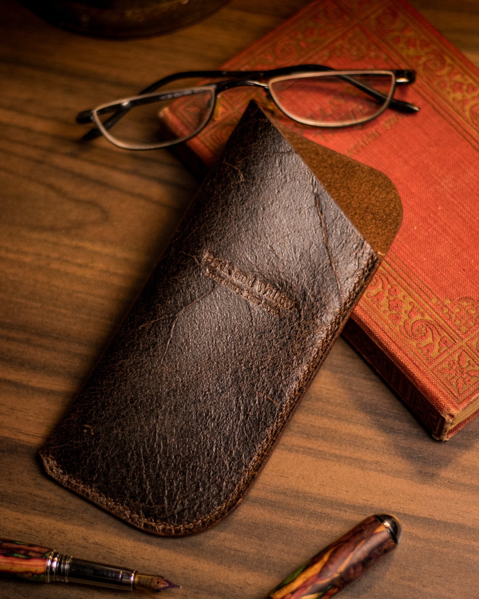 Lifestyle shot of a brown leather glasses case with a book and glasses