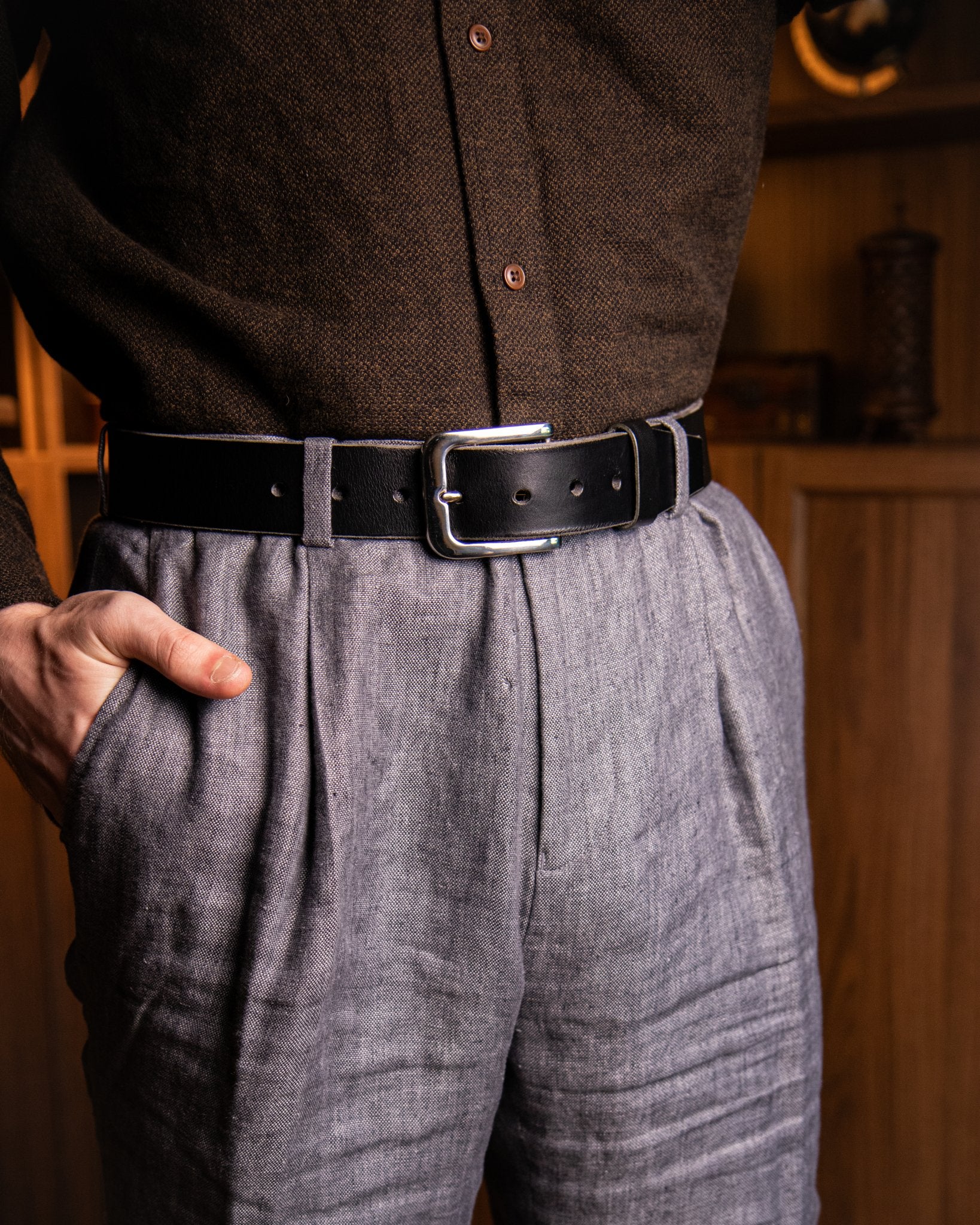 Person wearing a brown shirt and gray pleated pants with a black belt.