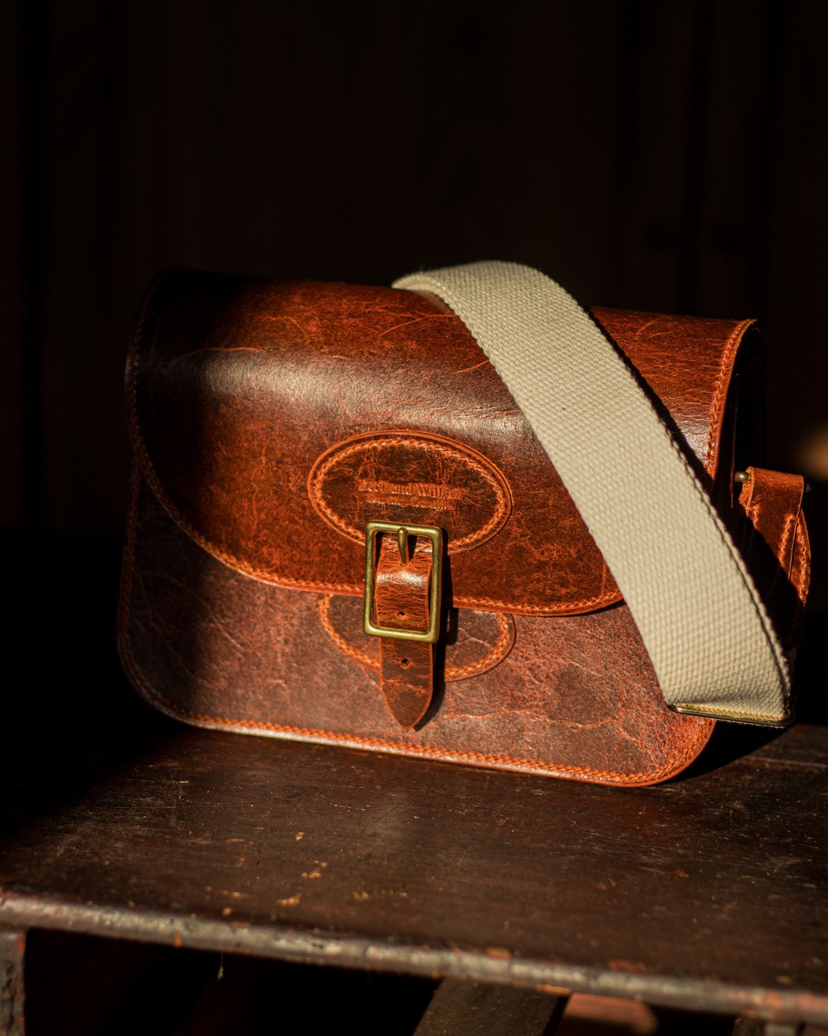 distressed tan leather bag sat in a ray of sun with its cotton strap