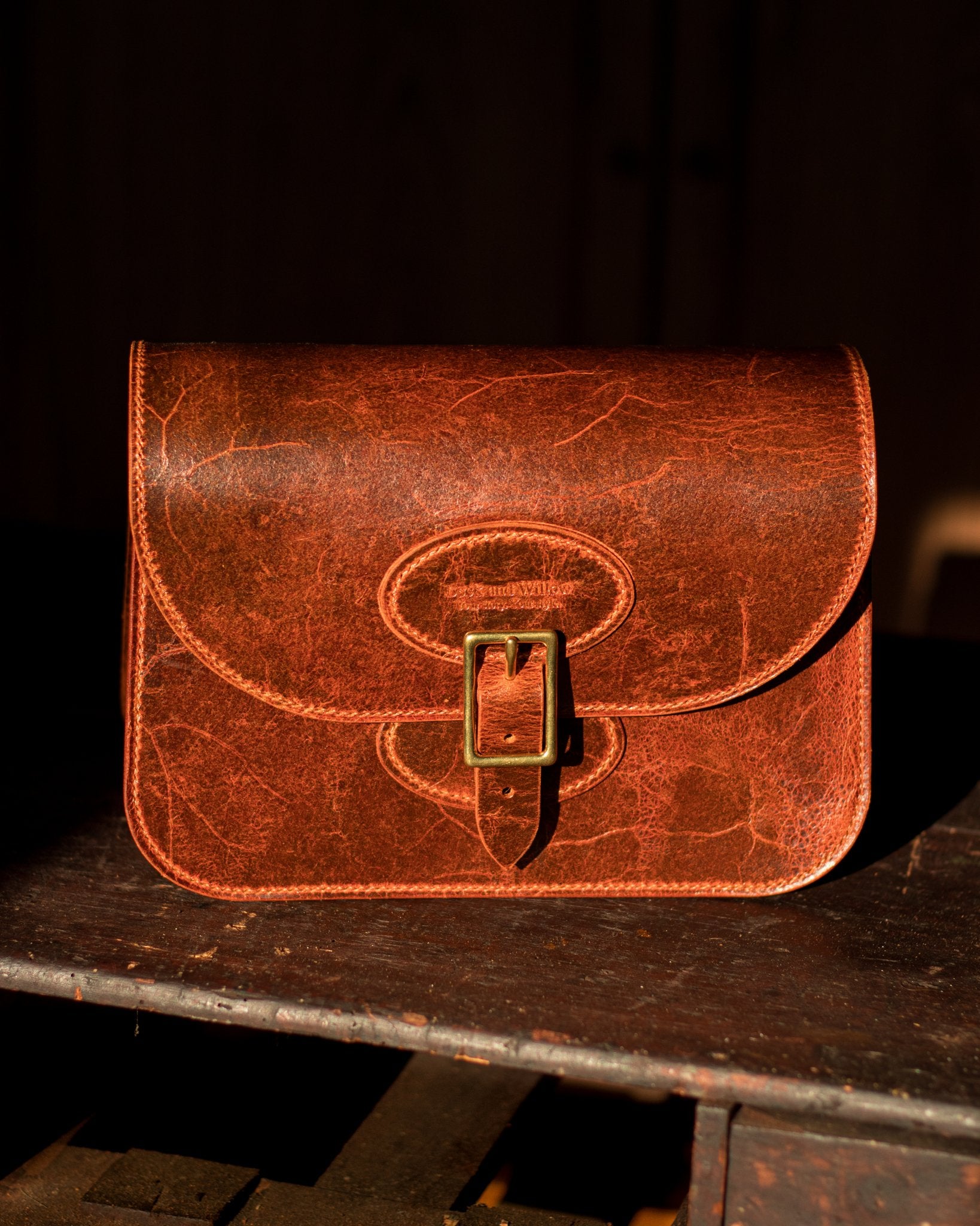 distressed tan leather crossbody bag with golden rays of sun hitting it