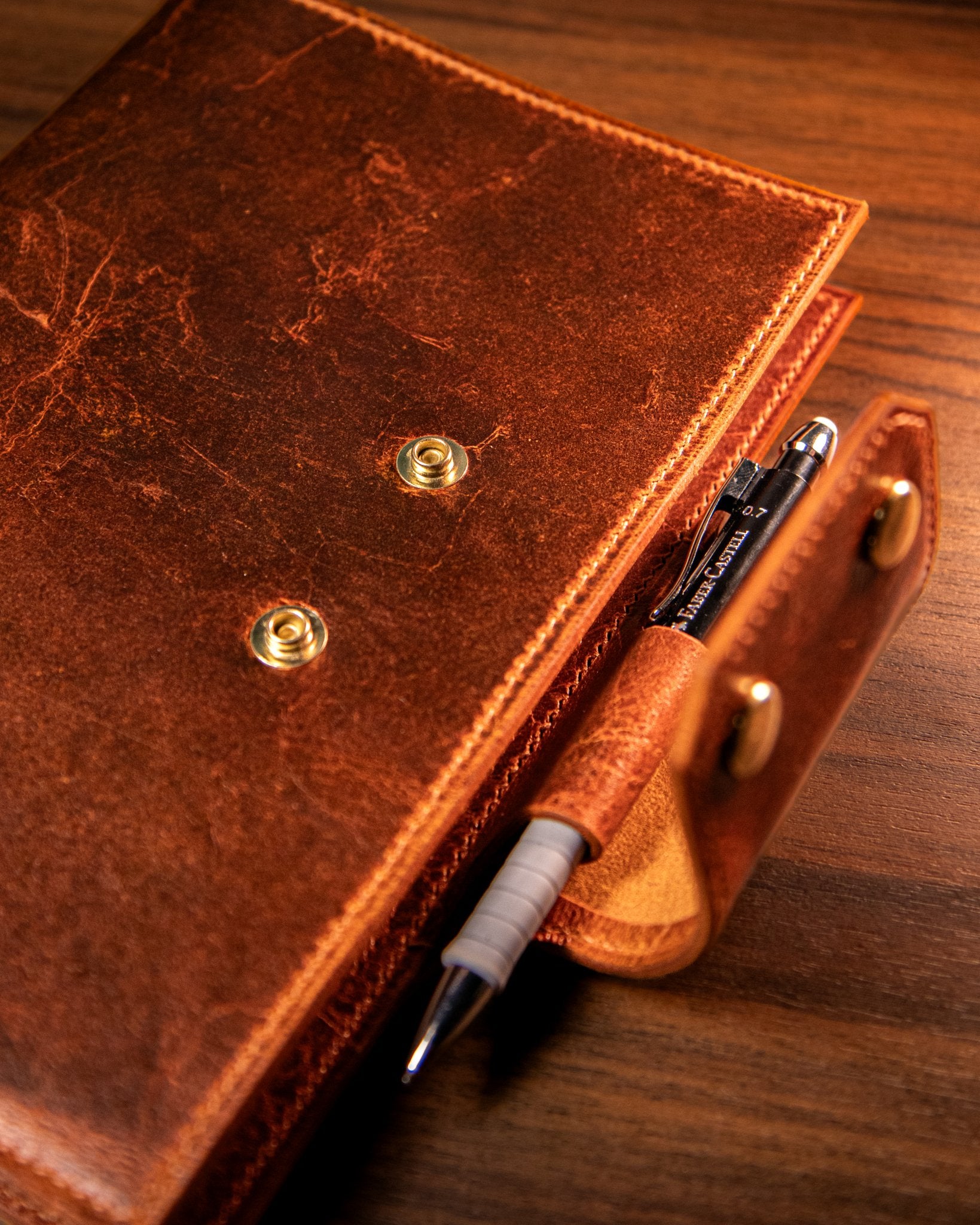 Tan leather notebook with a pen holder on a wooden surface