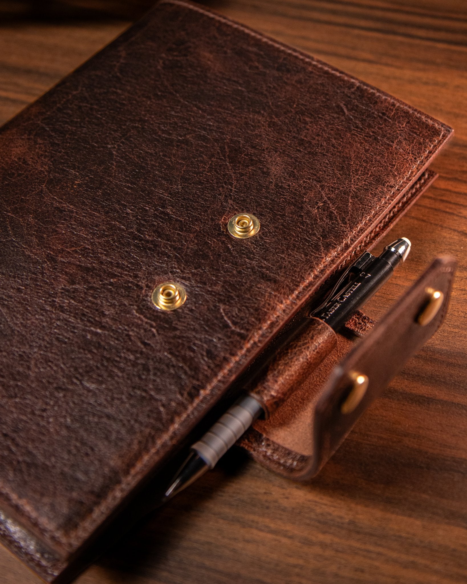 Brown leather notebook with pen holder on a wooden surface