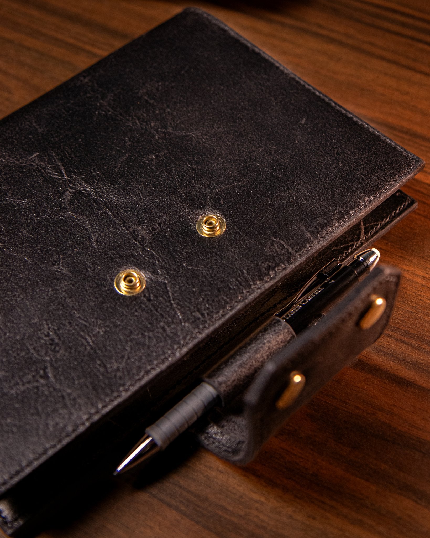 Close-up of a black leather notebook with gold poppers on a wooden surface