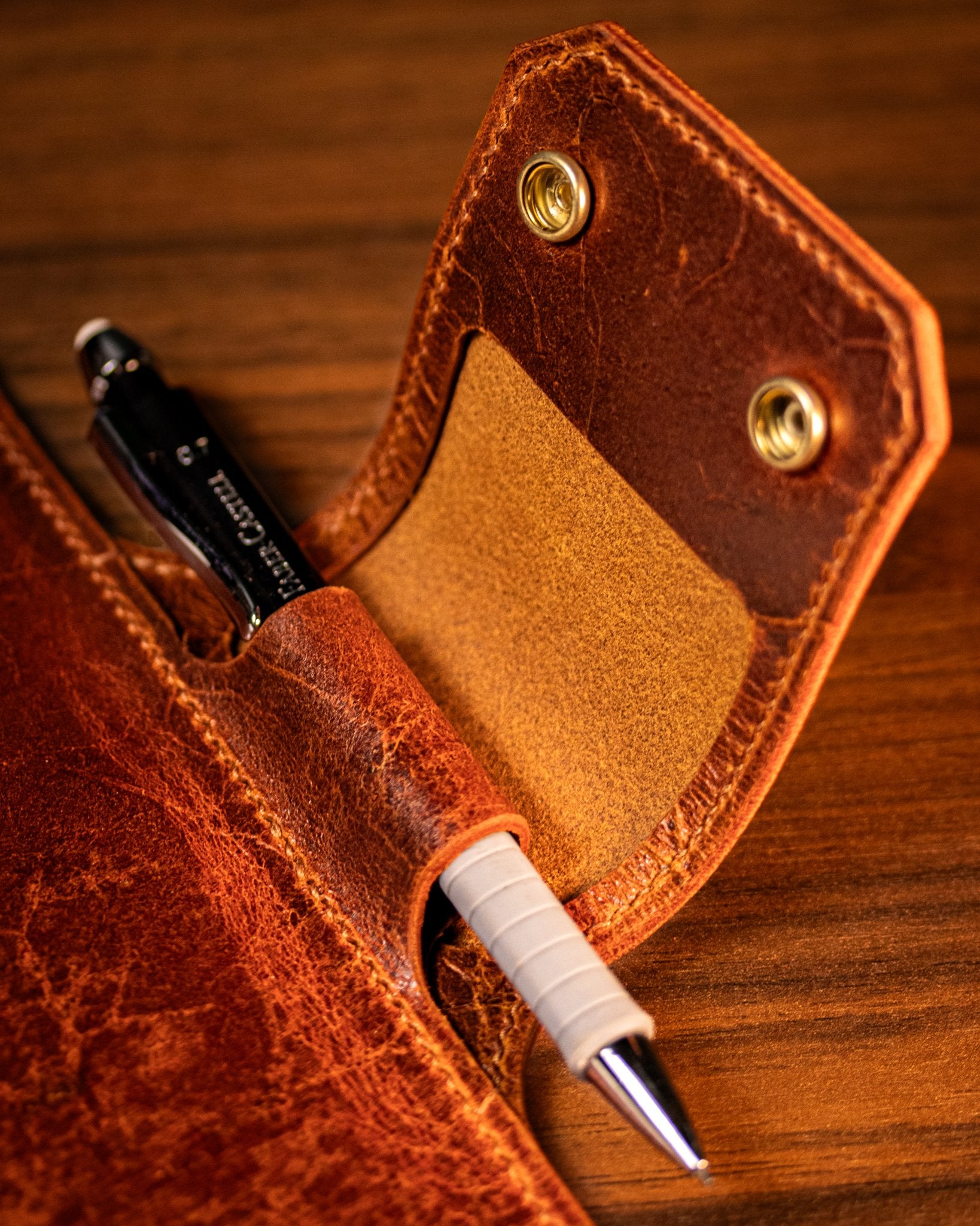 Tan leather pen holder for a journal with a pen on a wooden surface