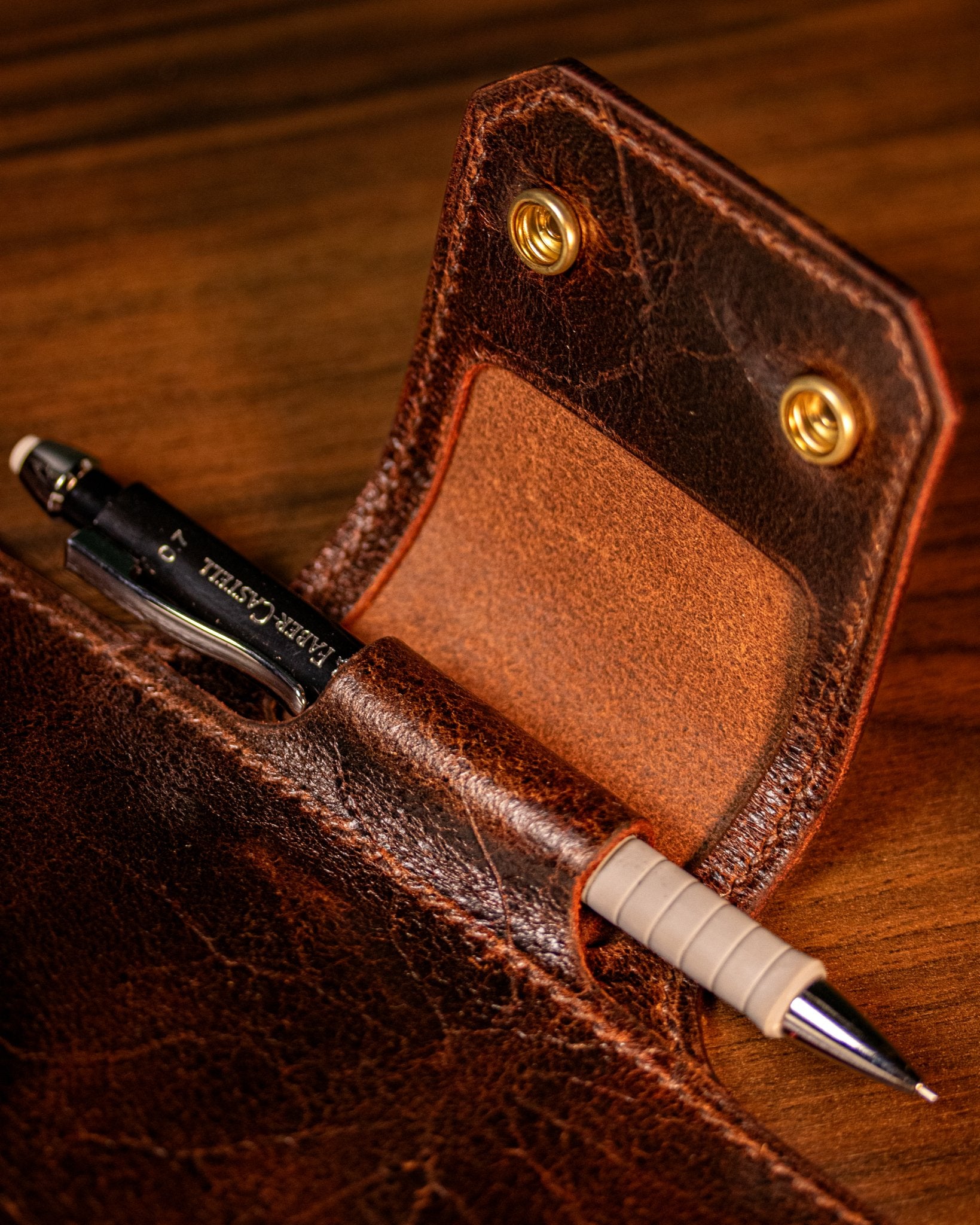 Brown leather pen holder in a journal with a pen on a wooden surface