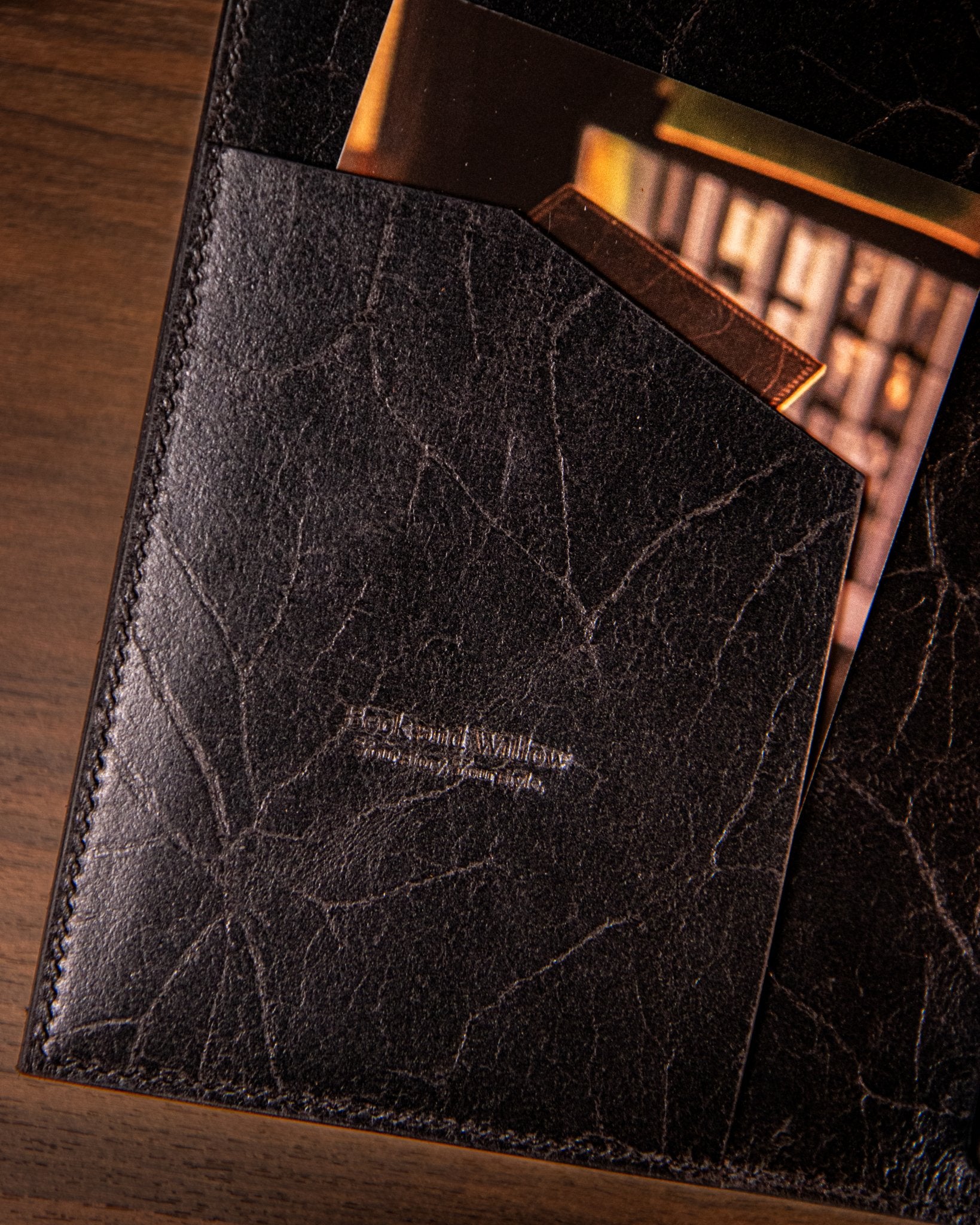 Black leather journal pocket with embossed logo on a wooden surface