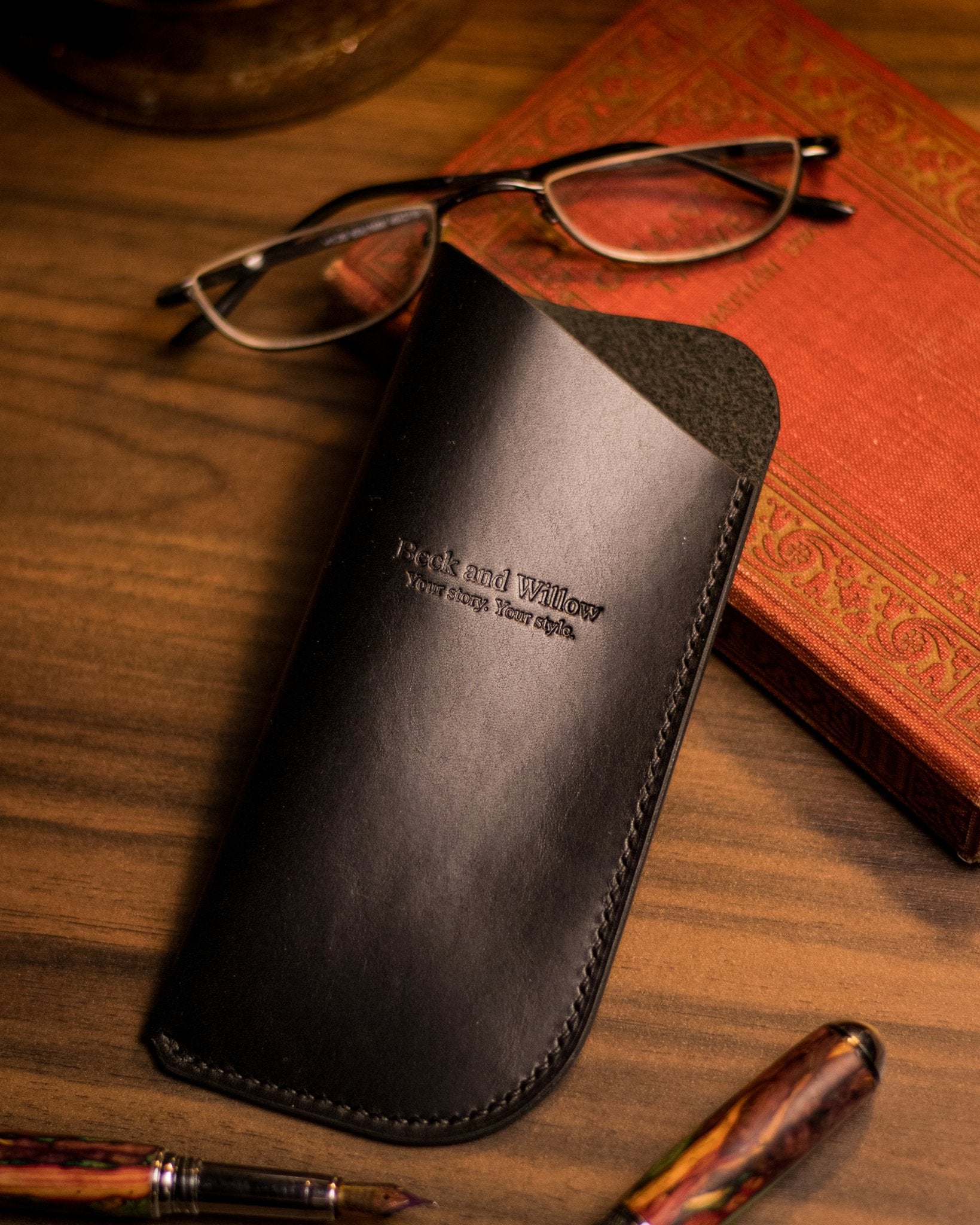 Lifestyle photo of a black italian leather glasses case with a book and glasses