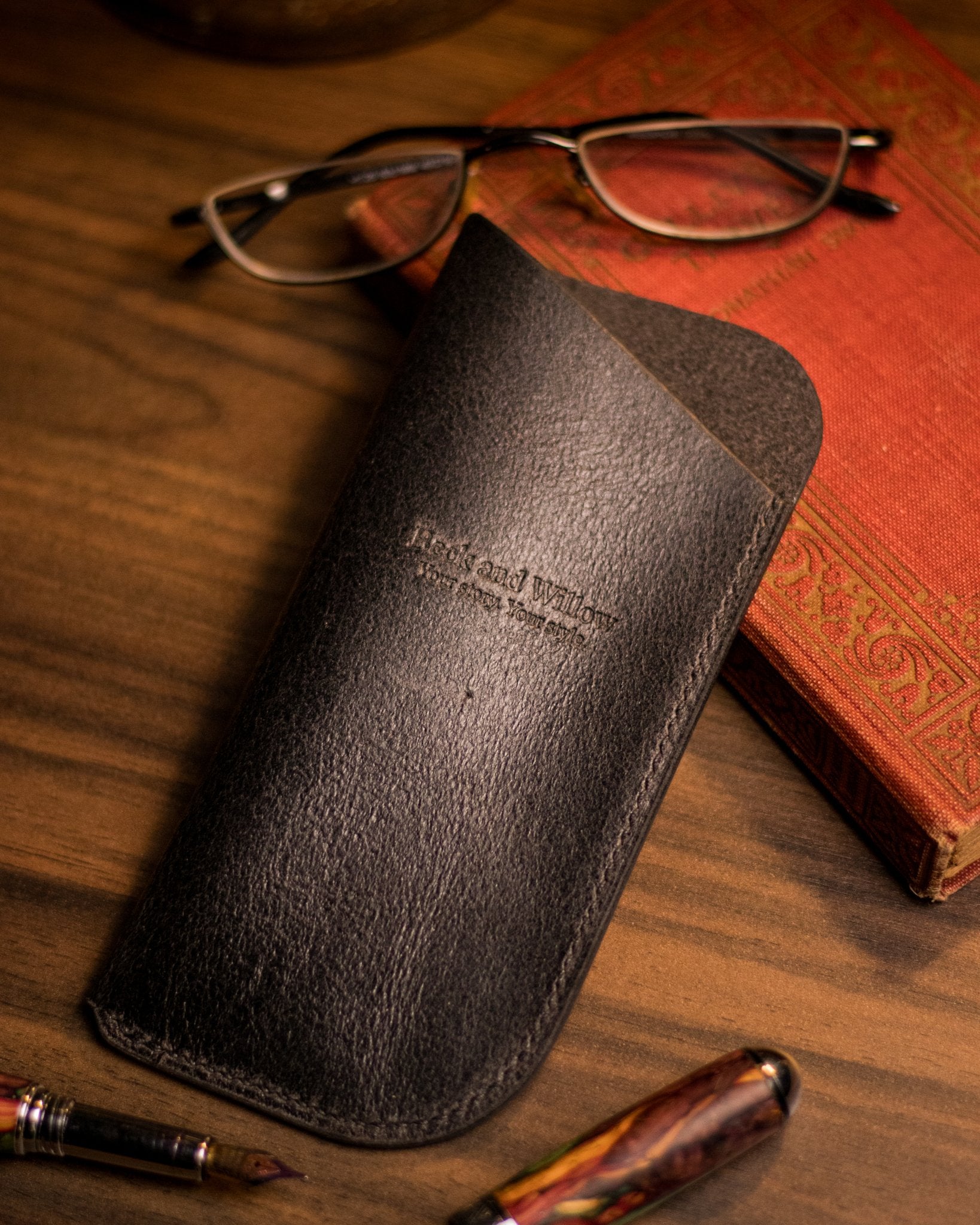lifestyle photo of a black leather glasses case with a book and glasses