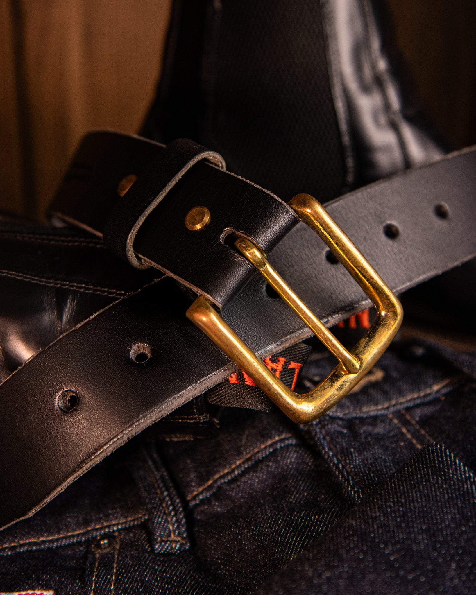 Black leather belt with a gold buckle on a dark background
