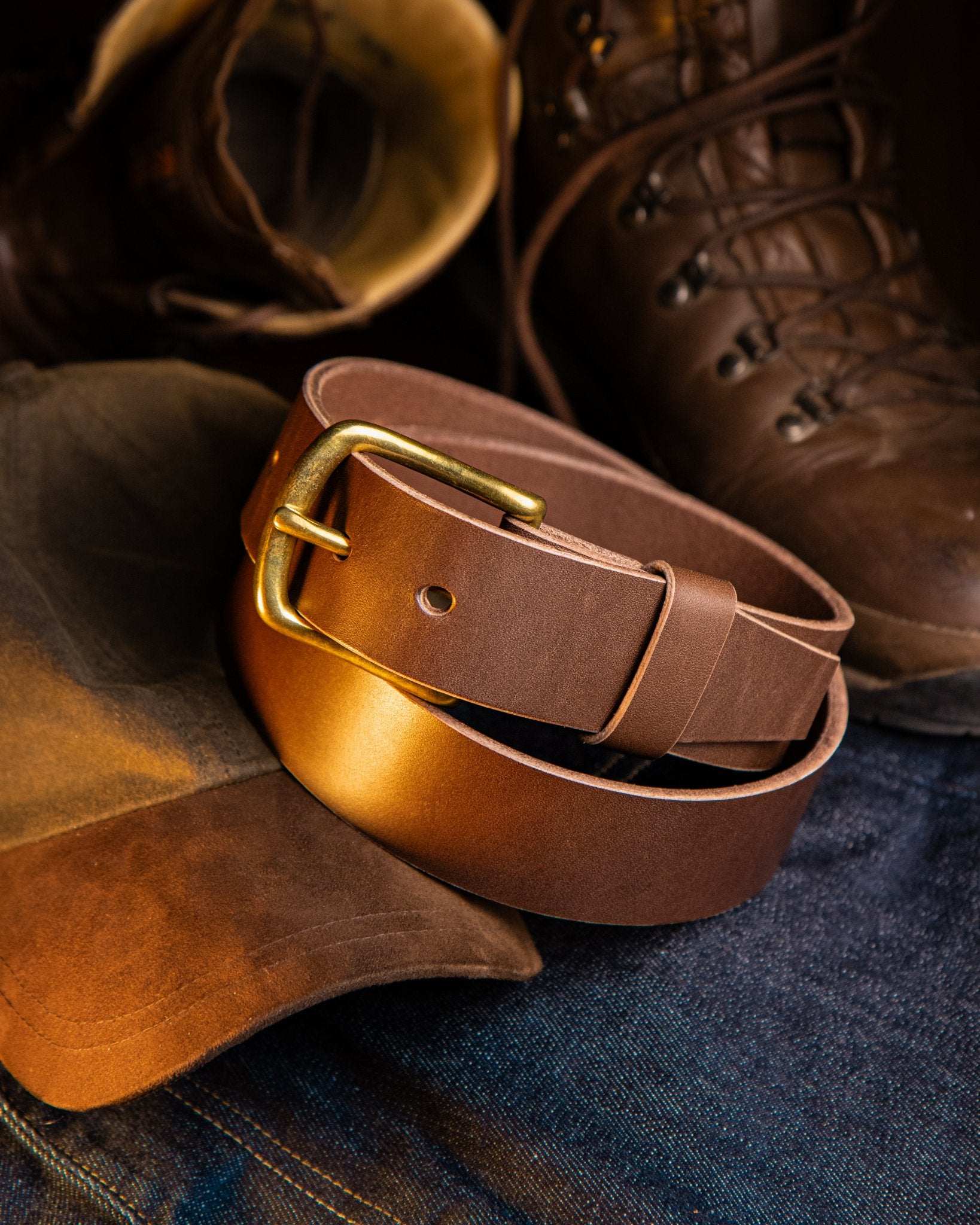 Brown leather belt with brass buckle on denim fabric, with brown boots in the background.