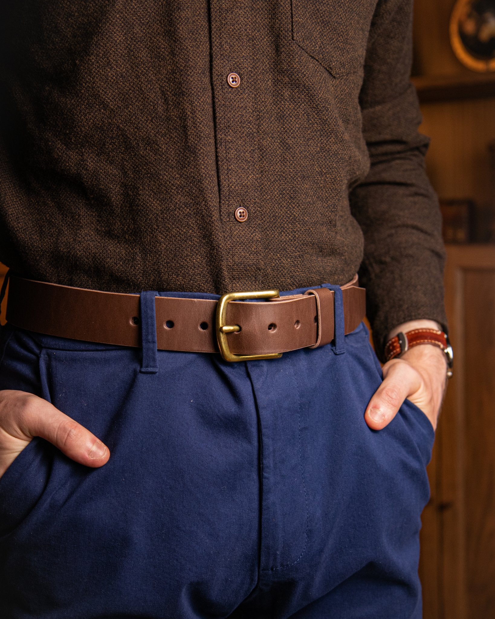 Person wearing a brown shirt, blue pants, and a brown belt with a gold buckle.