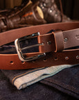 Brown leather belt with a silver buckle on a denim fabric background