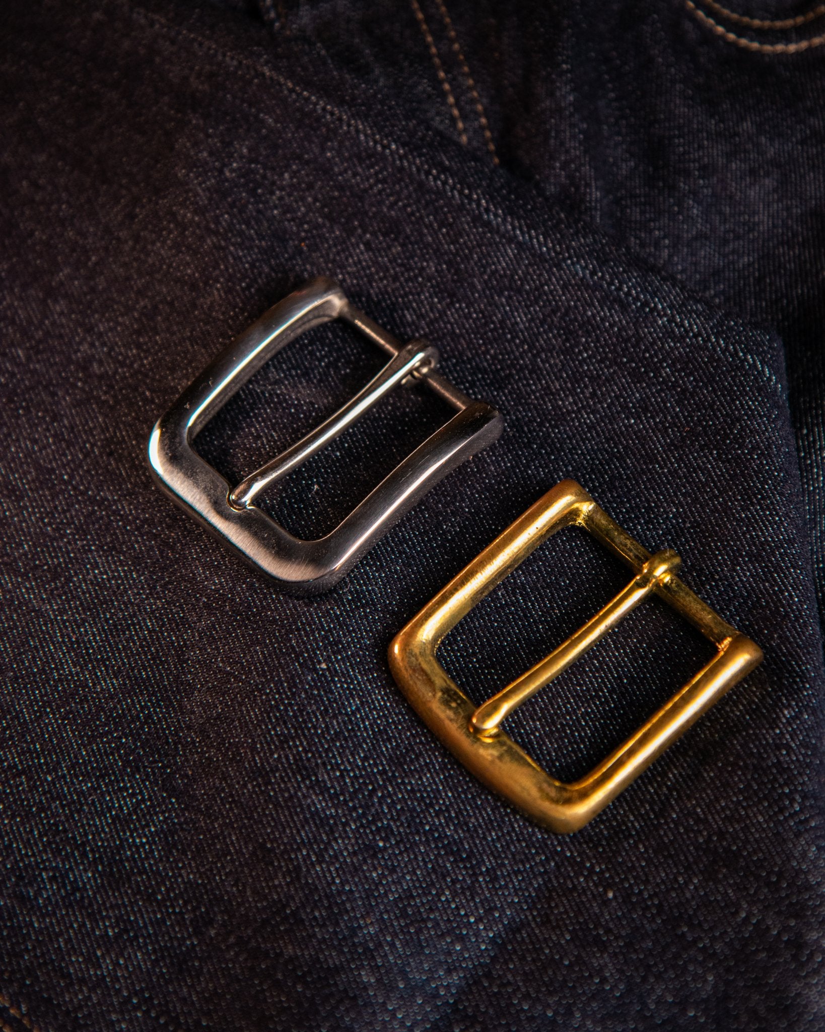 Two metal buckles, one silver and one gold, on a dark fabric background.