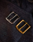 Two metal buckles, one silver and one gold, on a dark fabric background.