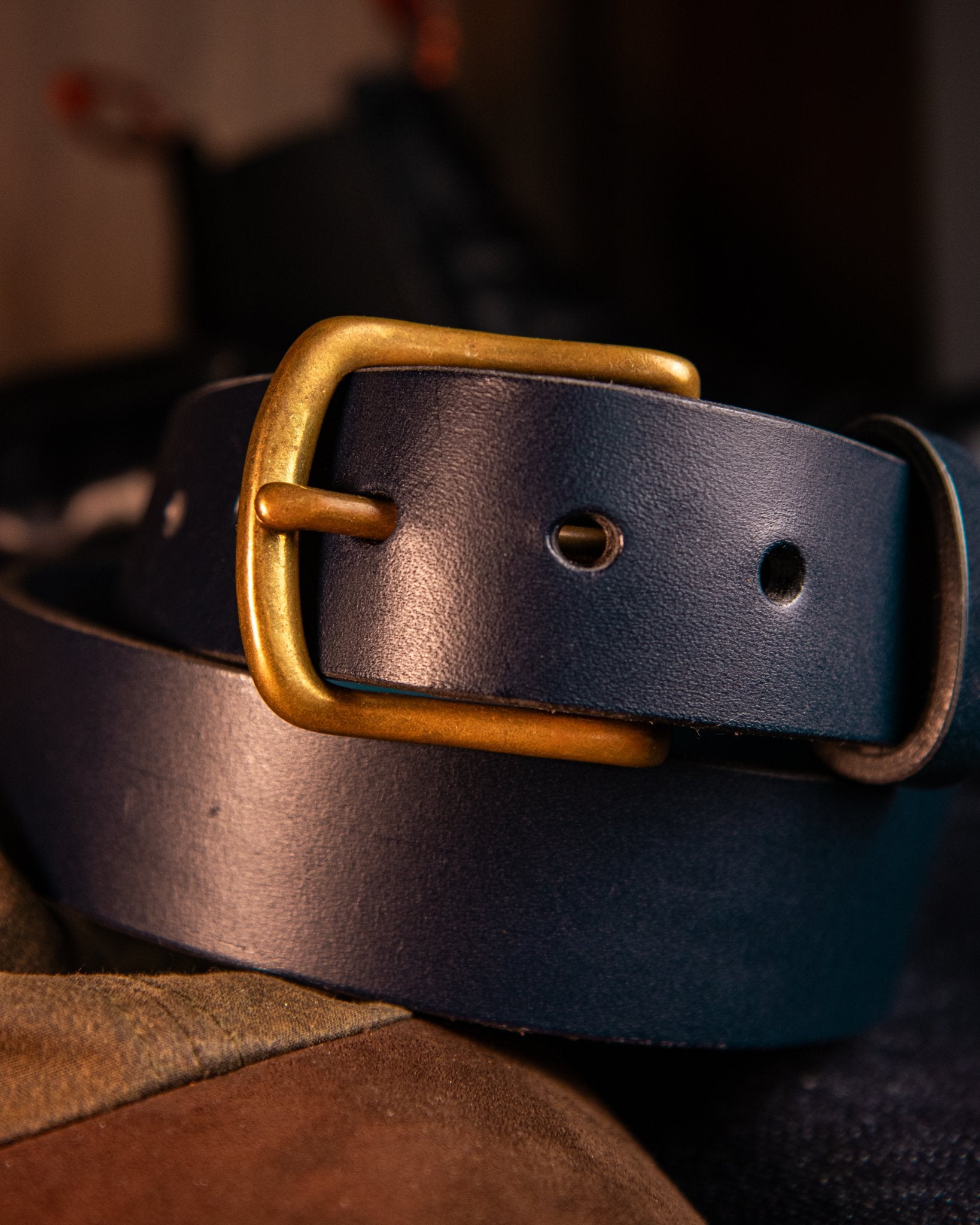 Dark leather belt with a brass buckle on a blurred background