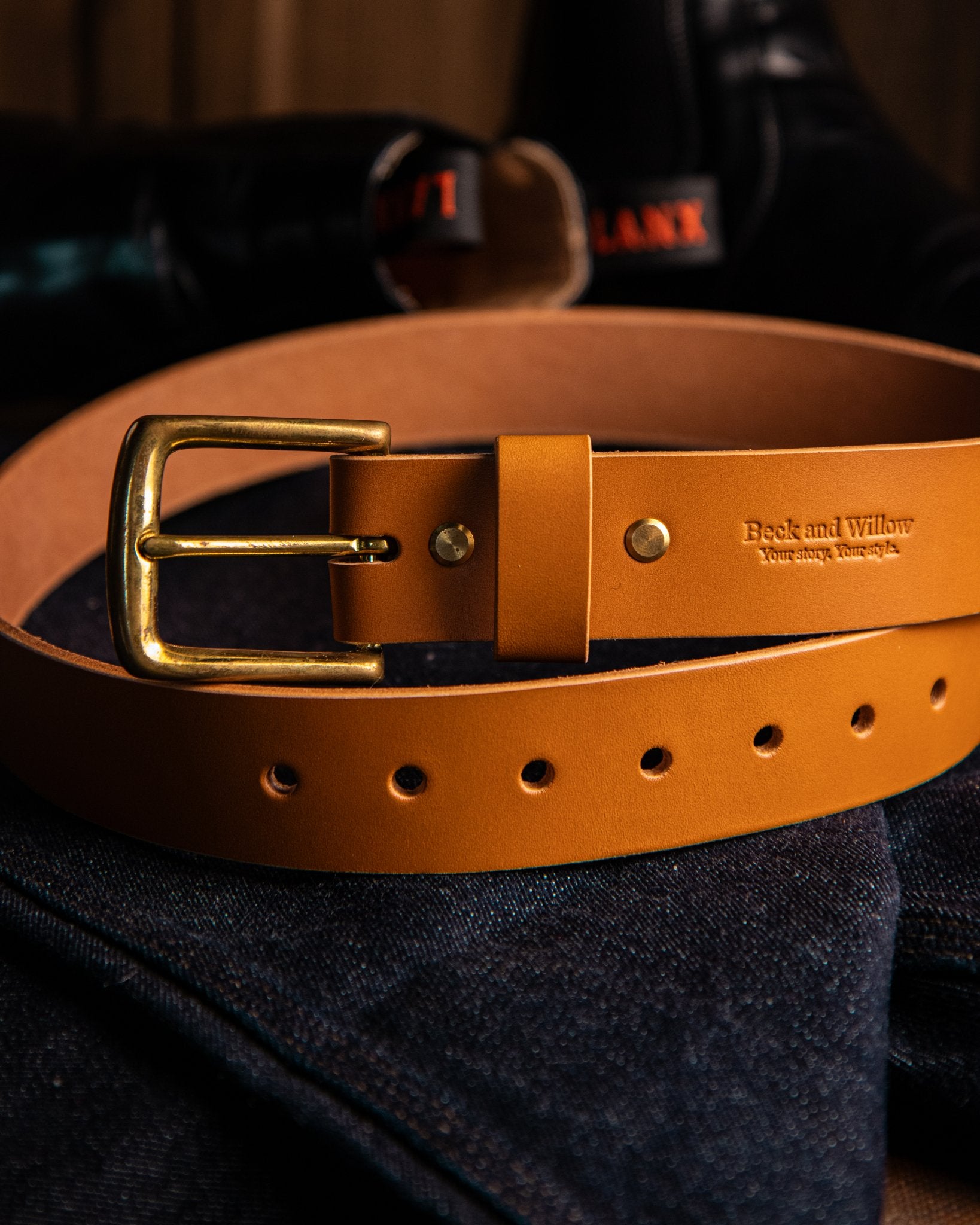 Tan leather belt with gold buckle on a dark fabric background