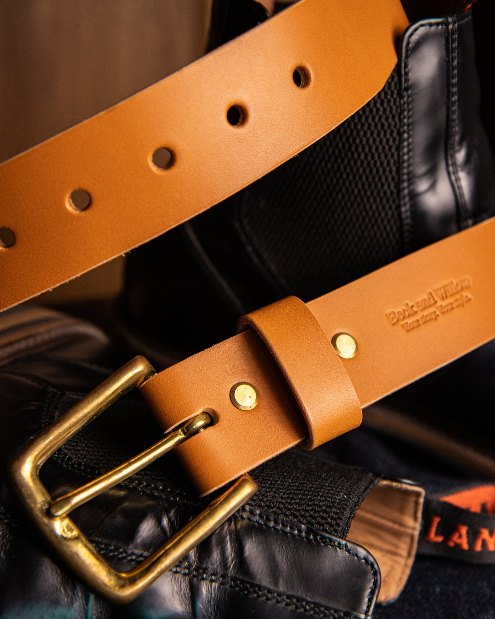 Tan leather belt with brass buckle on a black background