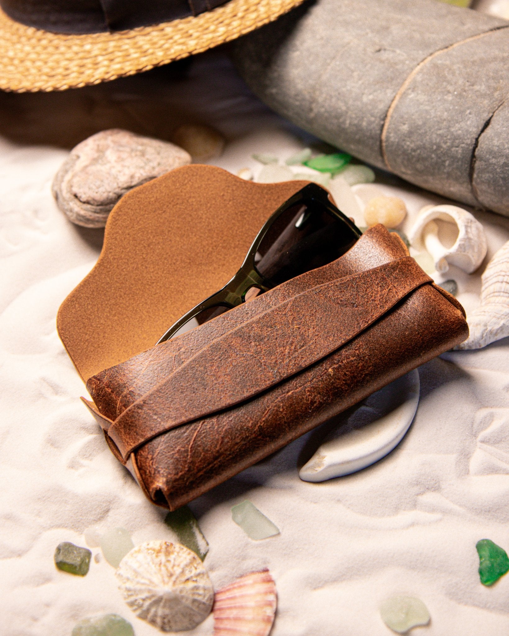 Tan leather Eyewear case on a beach with stones and shells.