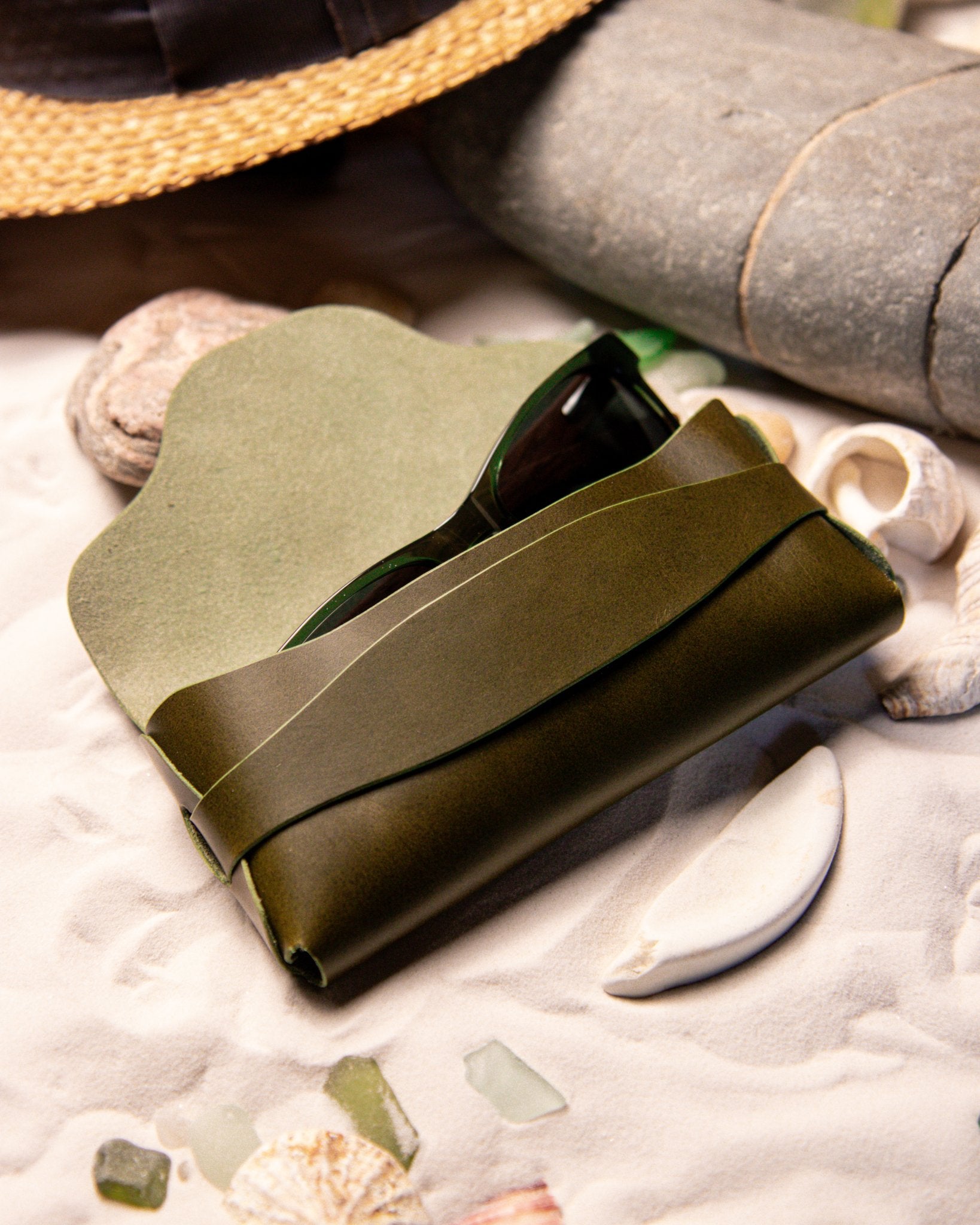 Olive green eyewear case on a textured surface with natural elements